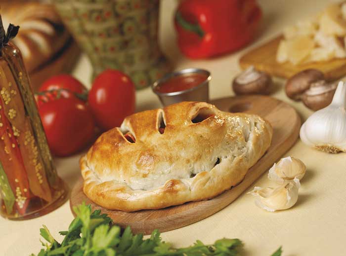 Calzone sitting on a cutting board near tomatoes